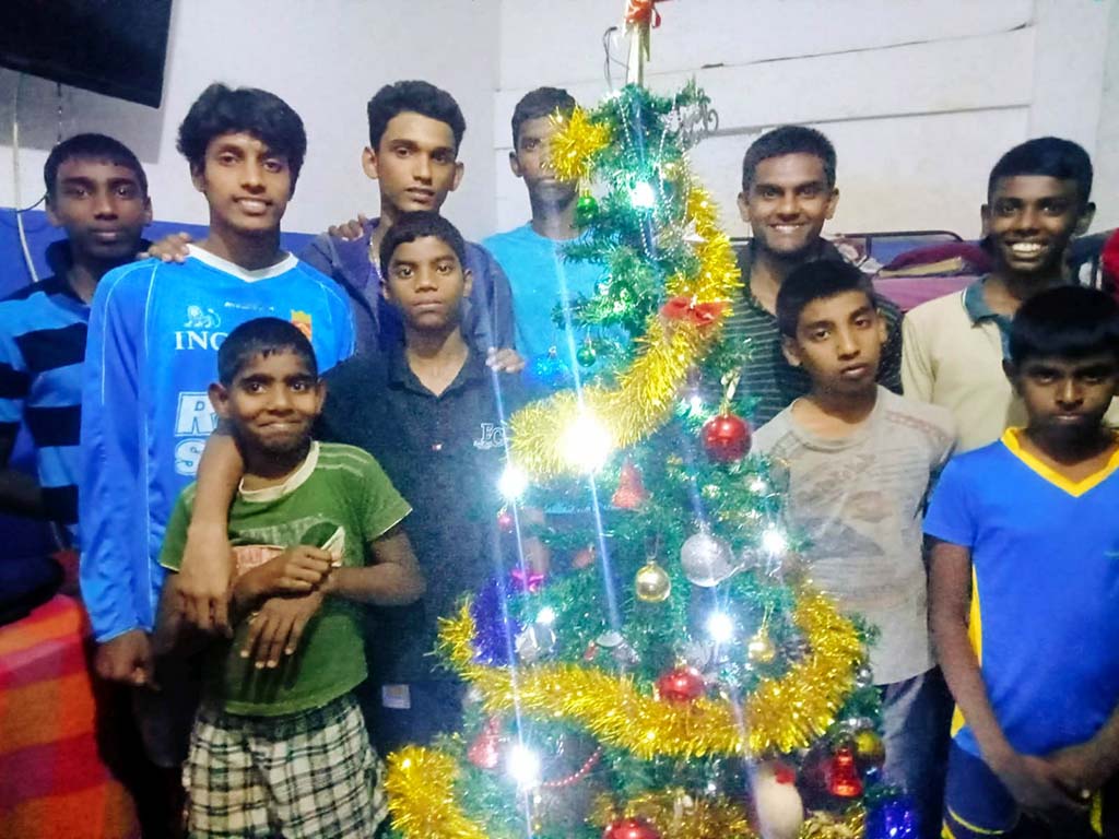 een aantal jongens staan bij de versierde kerstboom